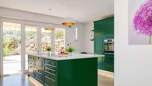 Une cuisine moderne dotée d’un îlot central, de meubles de rangement verts et d’une grande fenêtre offrant une vue sur l’extérieur.