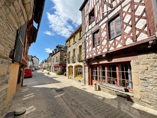 A narrow cobblestone street lined with traditional half-timbered buildings, a red car parked on the side, and a clear blue sky.