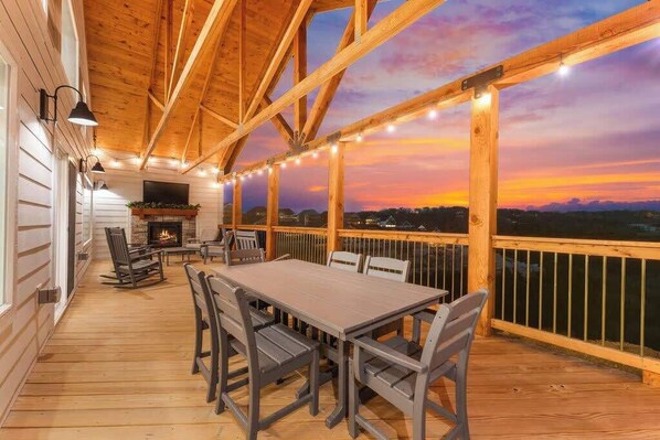 Una terraza de madera con una mesa, sillas, una chimenea y luces colgantes.