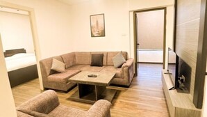 Ein modernes Zimmer mit Ecksofa, einem kleinen Tisch, einem Fernseher und einem Bett.