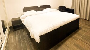 Ein modernes Schlafzimmer mit einem großen Bett, einem Nachttisch, einem Sessel und einem Fenster.