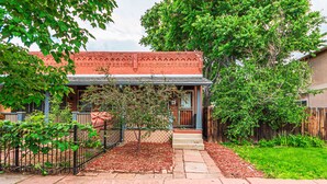 A single-story house with a red brick exterior, a front porch, and a small garden area with a fence and trees. - Cozy, Historic Home in A++ Location!! (Denver)