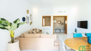 A modern living room with a beige sofa, a round wooden table, and a potted plant.