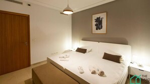 A hotel room with a large bed, a wooden door, a ceiling fan, and a framed artwork on the wall.