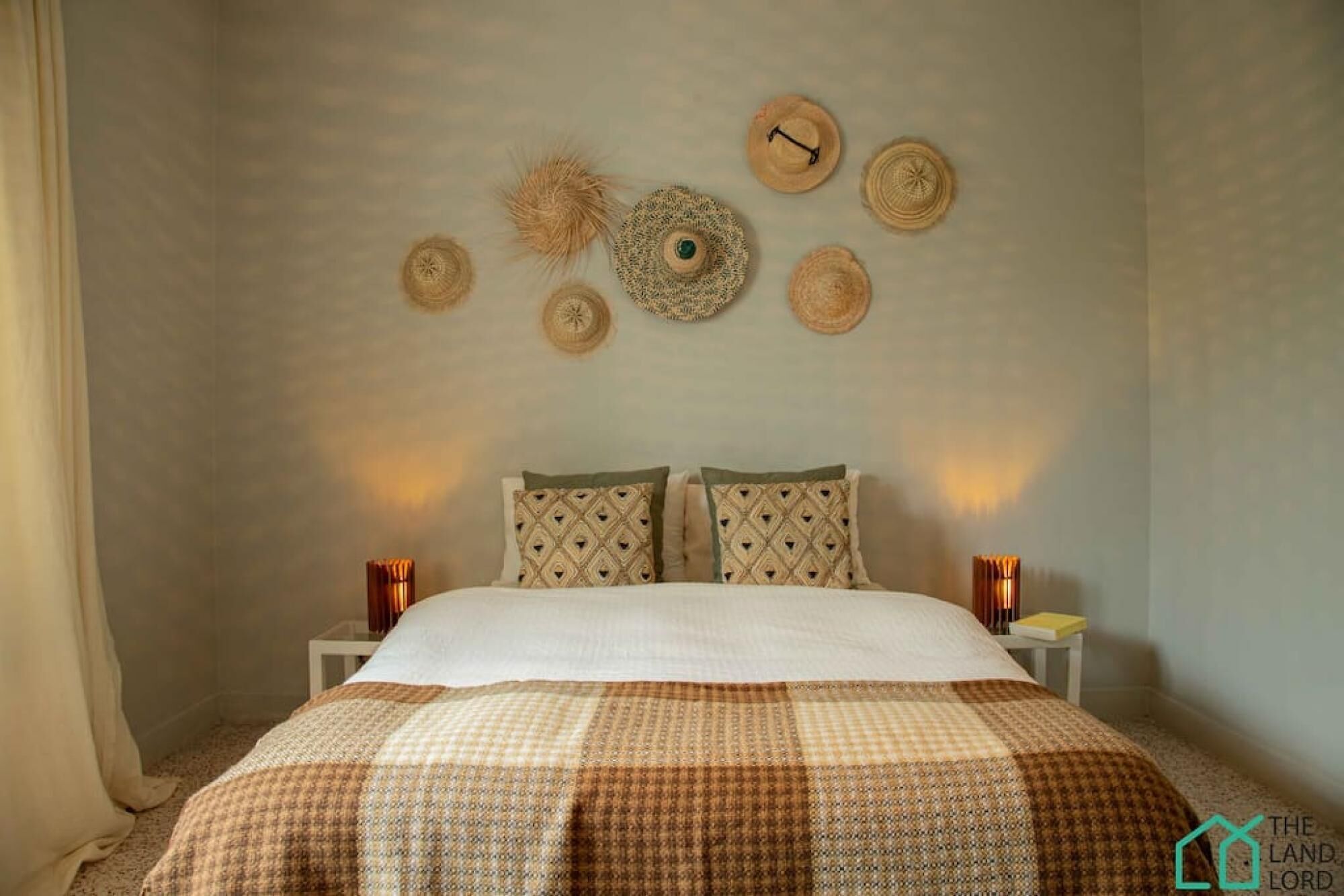 Une chambre à coucher comprenant un lit, deux tables de chevet et un mur décoré d’objets tissés.