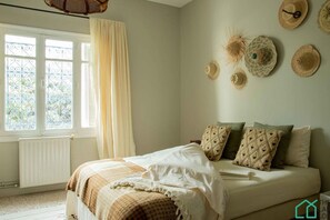 Une chambre à coucher avec un lit, une fenêtre avec des rideaux et des chapeaux décoratifs accrochés au mur.