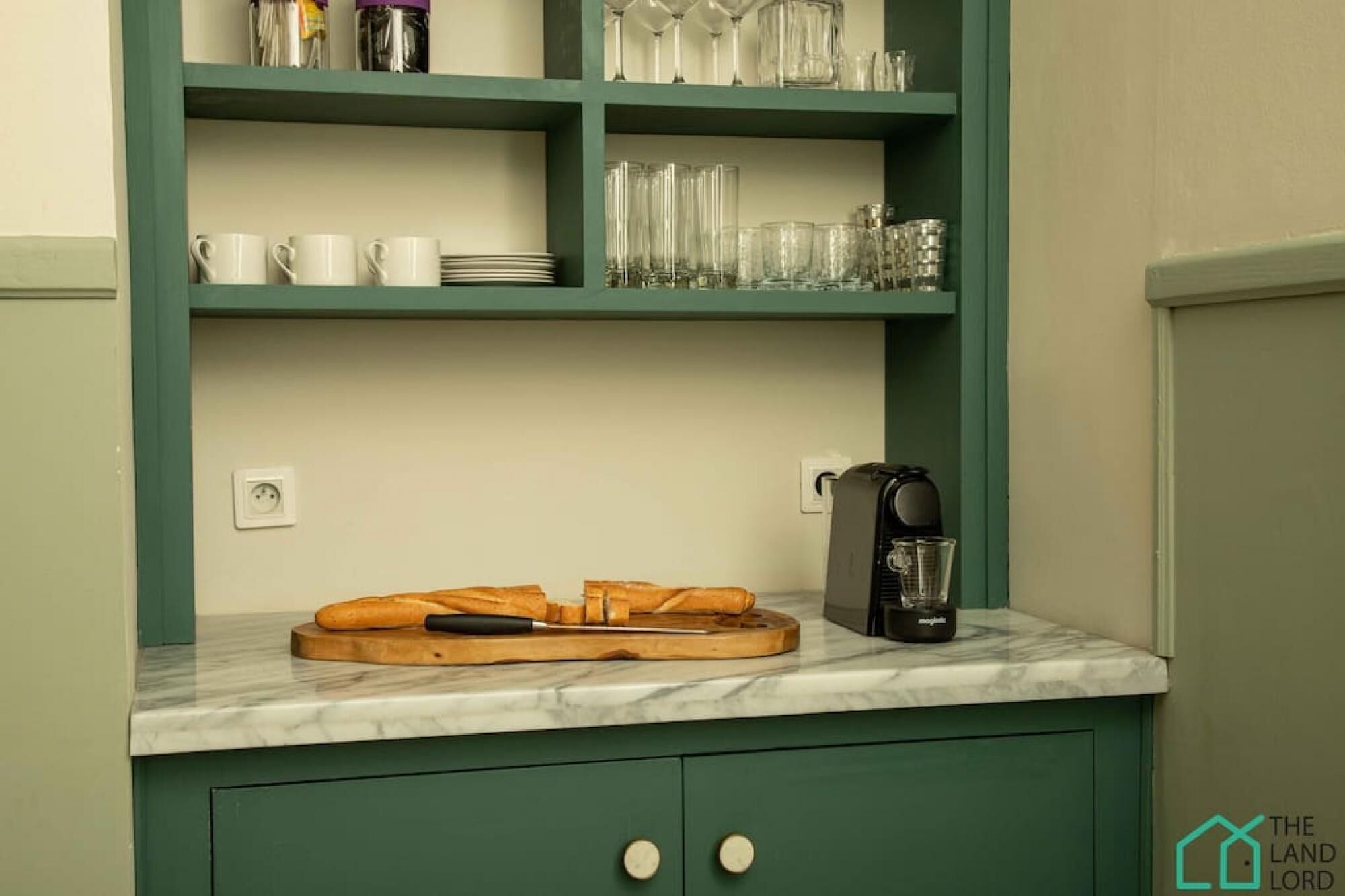 Une cuisine dotée d’un plan de travail en marbre, d’une machine à café et d’une planche à découper en bois avec un couteau.