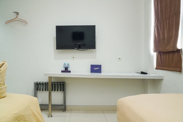 Habitación de hotel con cama, escritorio con televisor de pantalla plana, radiador y ventana con cortinas marrones.