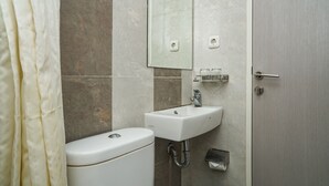 A bathroom with a toilet, sink, mirror, and shower curtain. - Singgahsini Rock Gubeng (Surabaya)