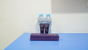A table with two water bottles and two boxes labeled "Sikat Gigi" on a blue table against a white wall. - Singgahsini Rock Gubeng (Surabaya)