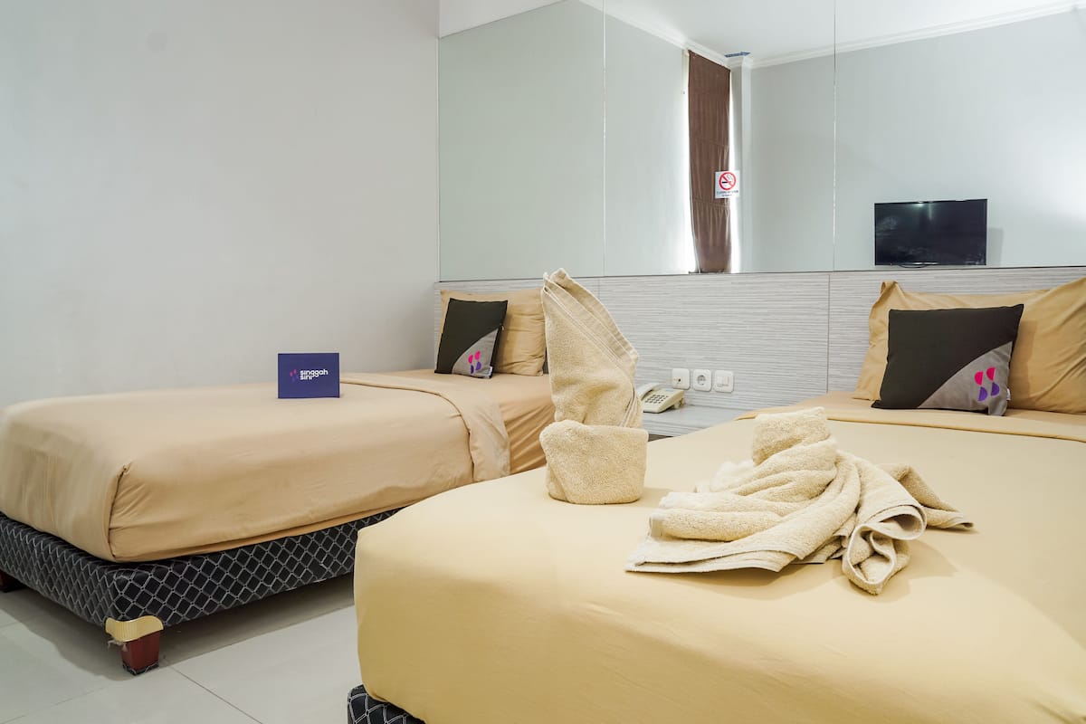 Une chambre d’hôtel avec deux lits, une literie de couleur beige, un grand miroir, une télévision et un panneau indiquant qu’il s’agit d’une zone non-fumeur.
