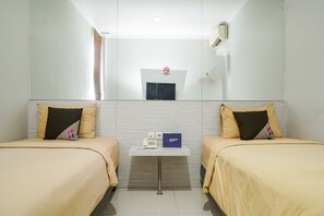 Habitación de hotel con dos camas, una mesita con un teléfono y un cartel, y un espejo en la pared.