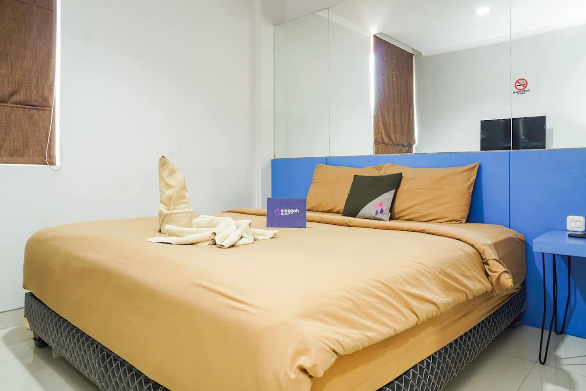 Une chambre d’hôtel avec un lit, une tête de lit bleue, une table de chevet et un miroir.