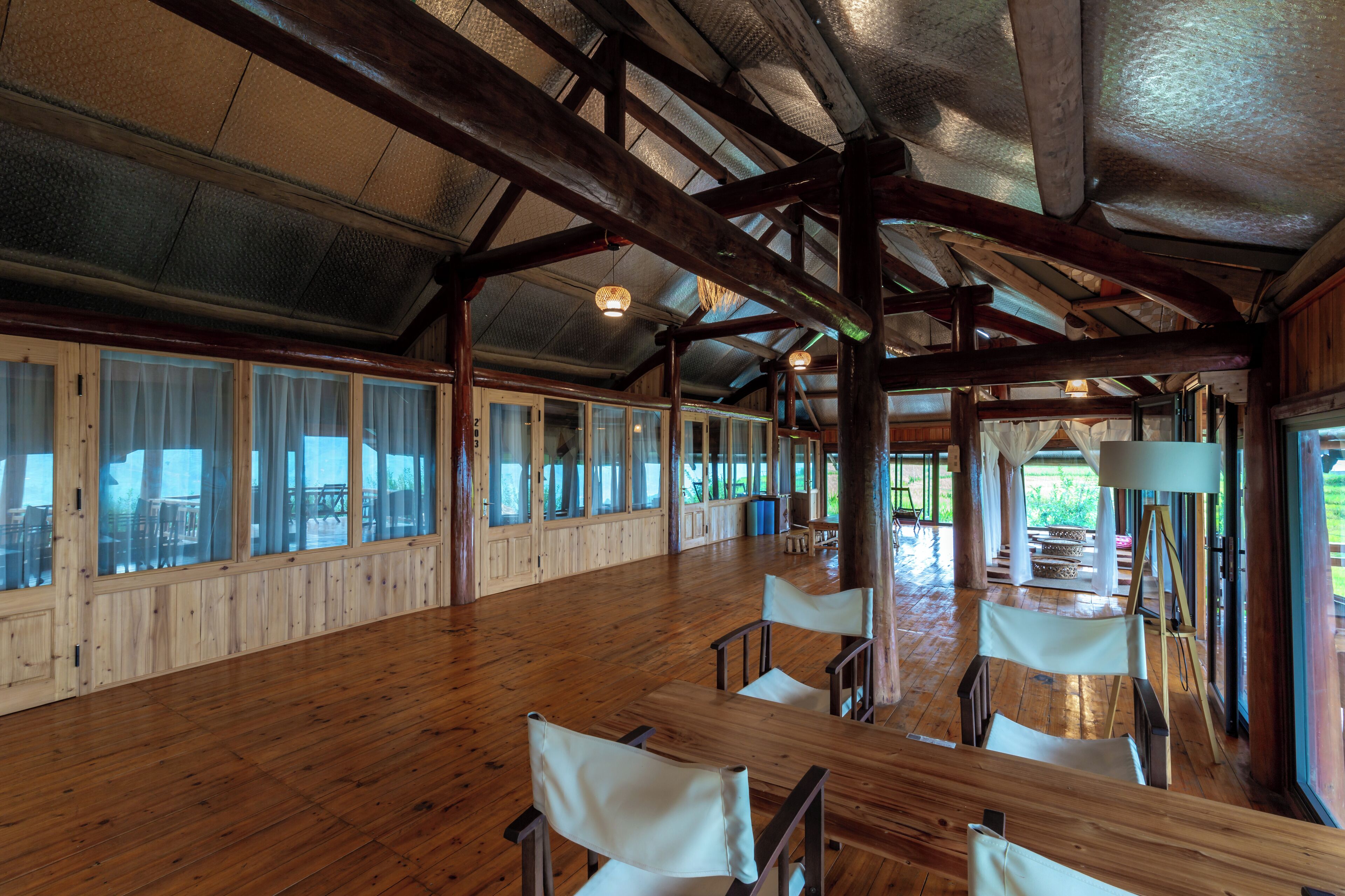 Un espacio interior amplio con pisos de madera y ventanas grandes, que incluye una mesa larga y varias sillas.