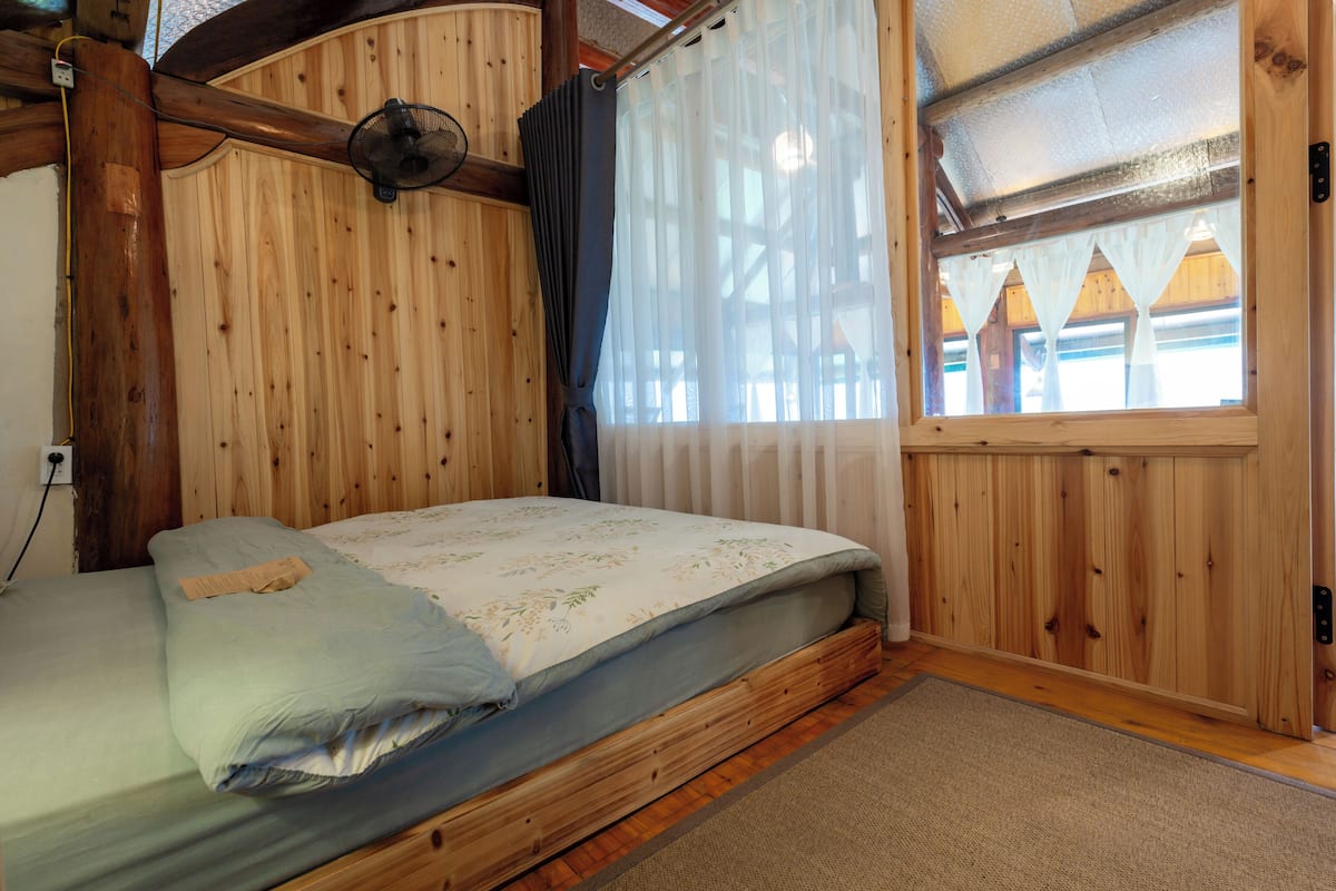 Quarto de cabana de madeira com cama, ventilador e janela com cortinas.