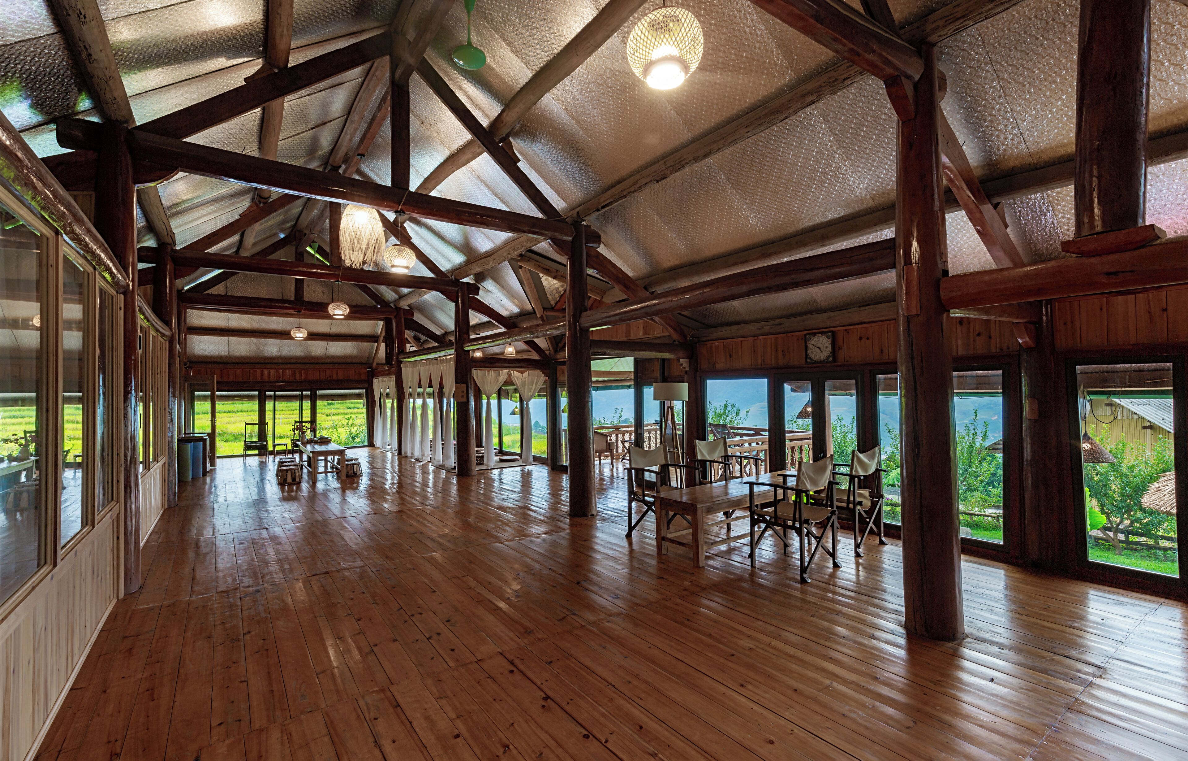 Amplio espacio interior con pisos de madera y ventanas grandes que ofrecen vistas a un paisaje verde.