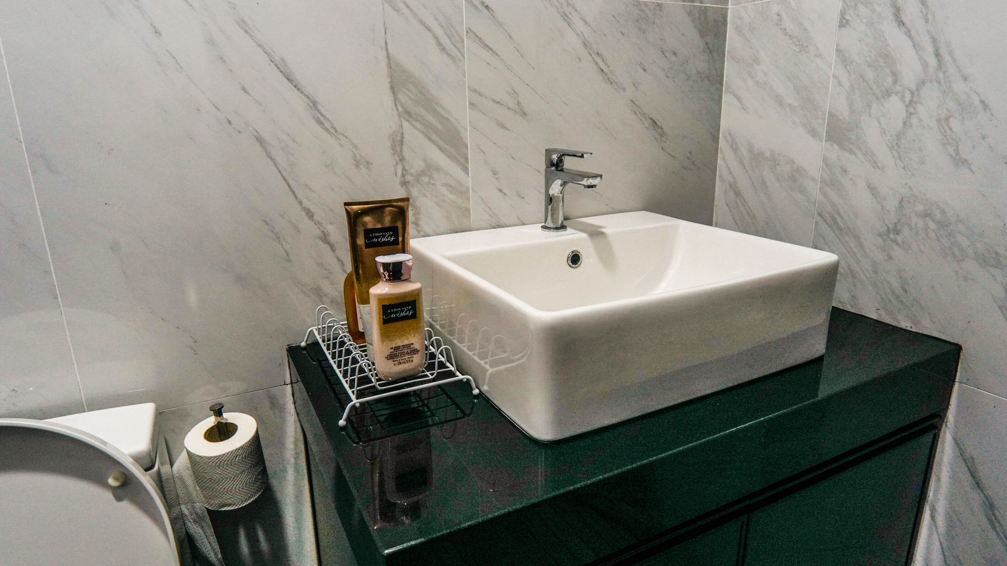 A bathroom with a white sink, a mirror, and toiletries on a shelf.