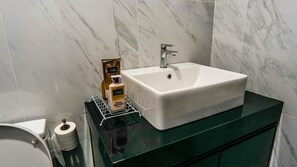 A bathroom with a white sink, a mirror, and toiletries on a shelf. - Emporis SOHO Residence by Airhost  (Petaling Jaya)