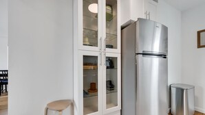 Une cuisine moderne avec un réfrigérateur en acier inoxydable, un meuble intégré doté de portes en verre et un petit tabouret.