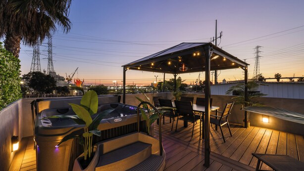 Une terrasse sur le toit avec un jacuzzi, des sièges d’extérieur et une pergola illuminée de guirlandes lumineuses.