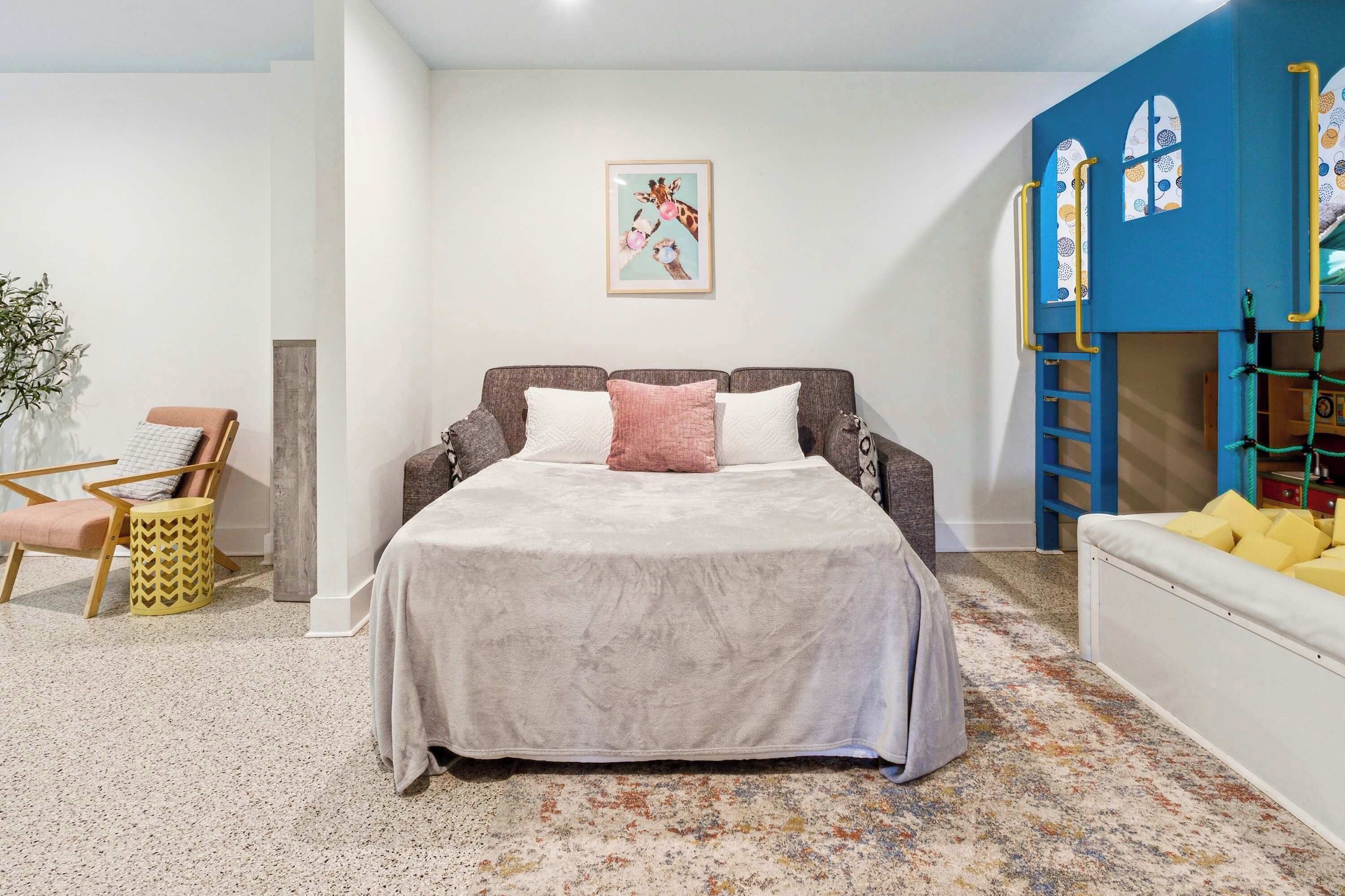 Un dormitorio con cama, una silla, una mesita y una pared azul con ventanas.