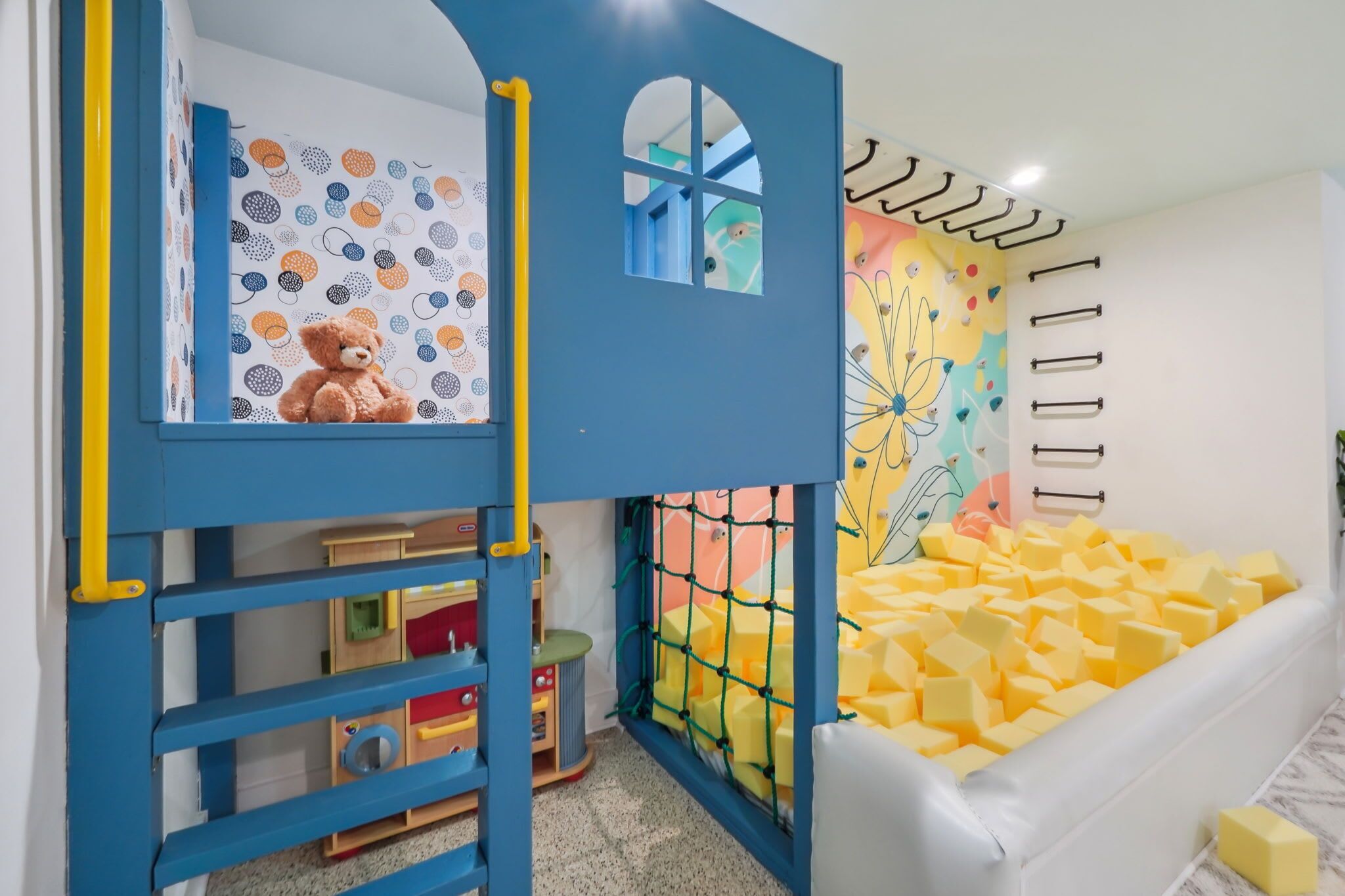 Zona infantil con una cama alta, una escalera y un colchoneta acolchada.