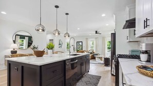 A modern kitchen with a central island, black cabinets, stainless steel appliances, and pendant lighting.
