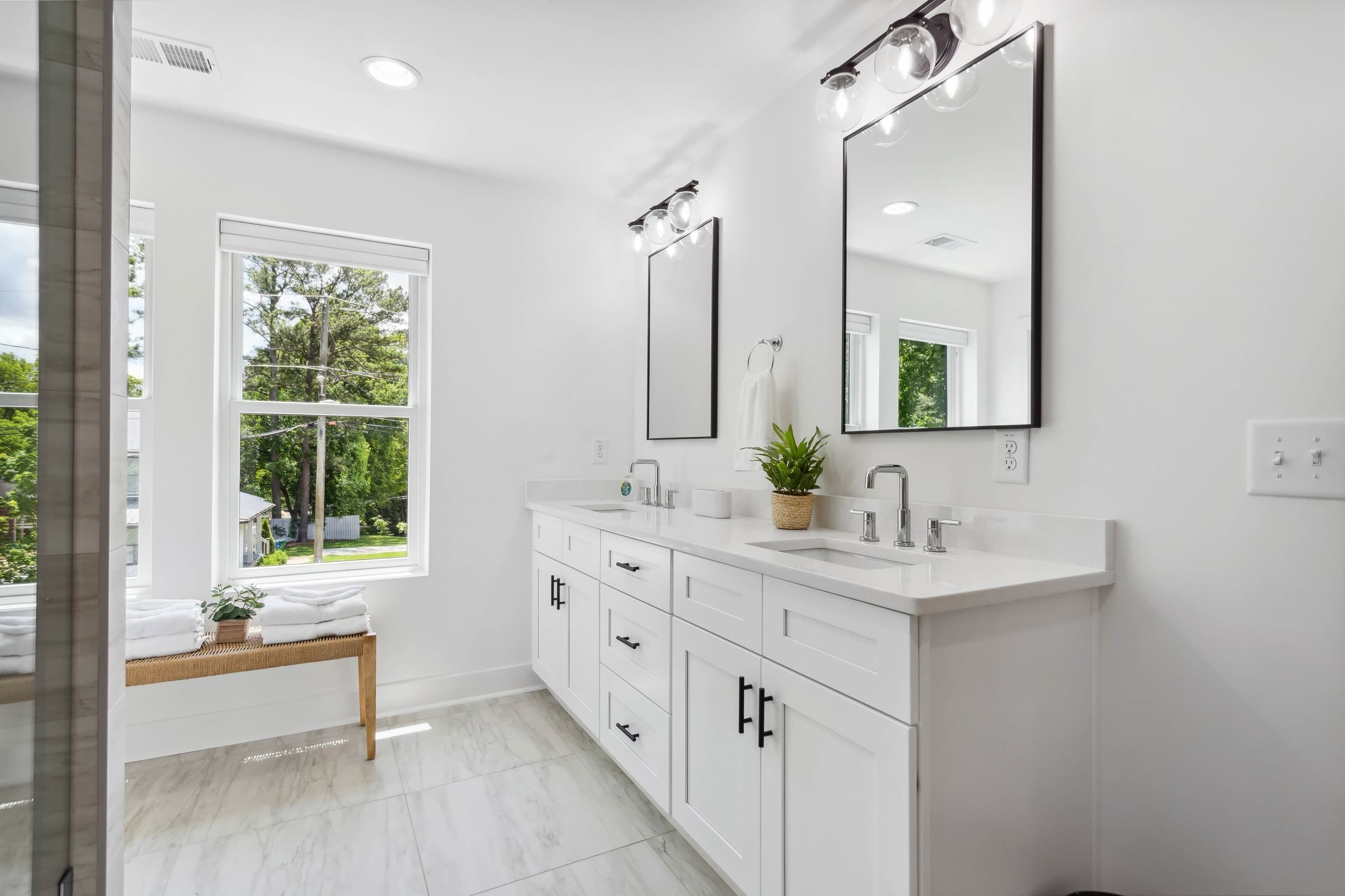 A modern bathroom with white fixtures, a large window, and a bench with towels.