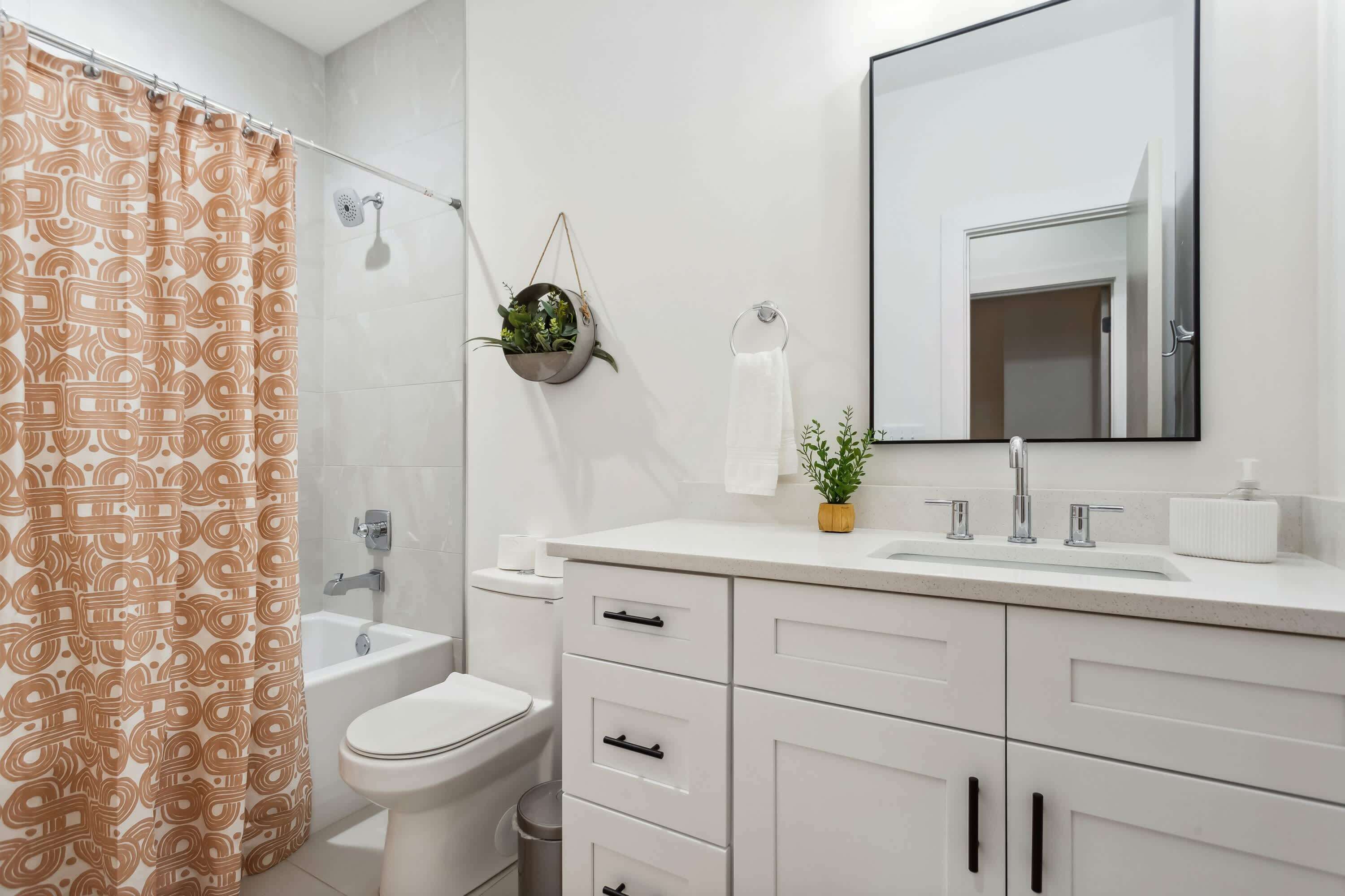A modern bathroom with a shower curtain, toilet, sink, and cabinets.