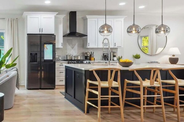 A modern kitchen with white cabinets, a black island, and wooden chairs.