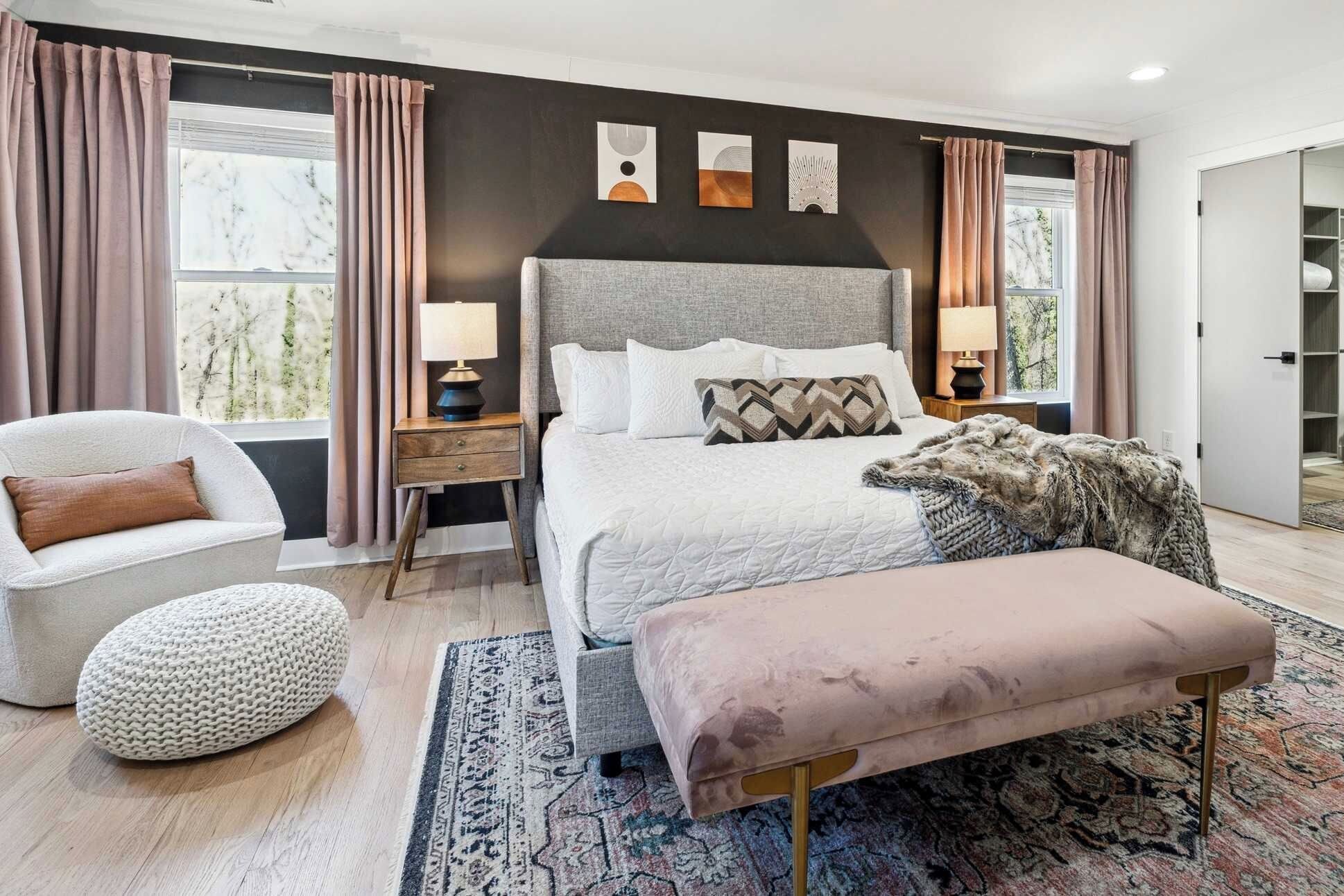 A modern bedroom with a large bed, bedside lamps, a chair, a bench, and artwork on the wall.