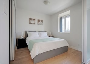 Un dormitorio con cama, mesitas de noche, un ventanal y dos obras de arte en la pared.