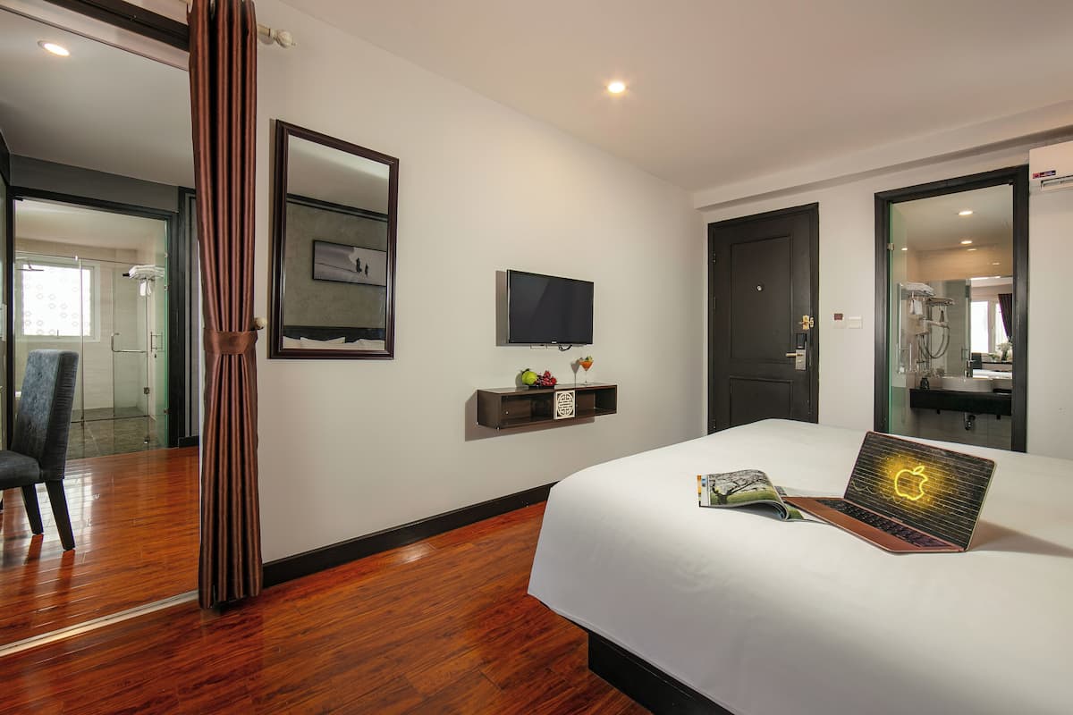 A hotel room with a bed, a television, a small shelf with decorative items, and a mirror.