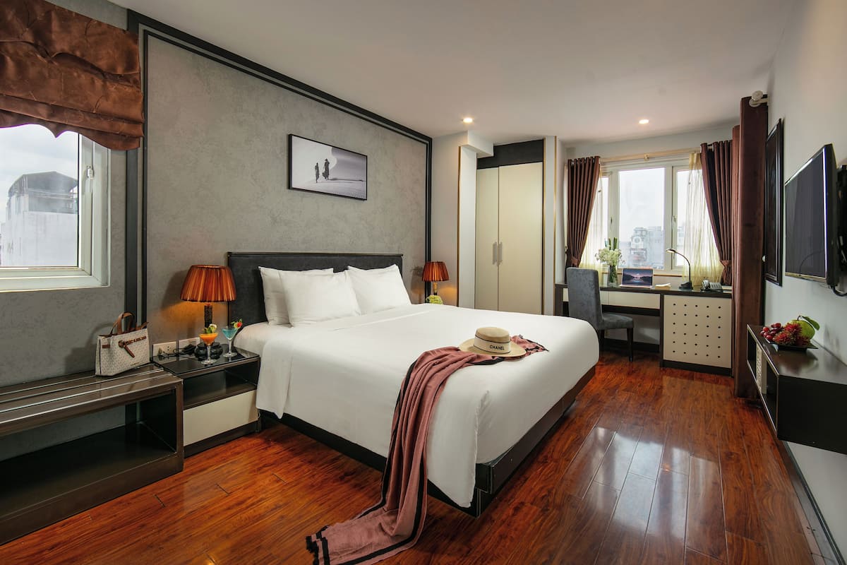 A hotel room with a large bed, a desk, a chair, a TV, and a window with curtains.