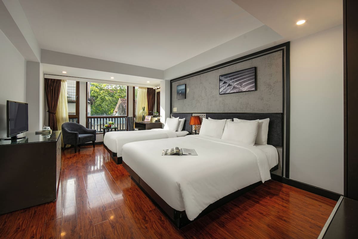 A hotel room with two beds, a desk, a TV, and a balcony with curtains.
