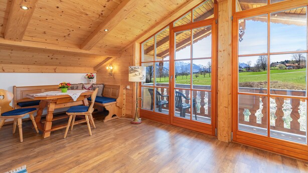Un interior de madera con comedor, ventanas amplias y vistas a un paisaje verde.