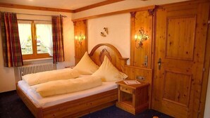Una cama de madera con dos almohadas, una mesita de noche y un armario de madera en una habitación con ventana y cortinas.