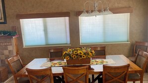 A dining area with a wooden table and chairs, a flower centerpiece, and two windows with blinds. - FUN FAMILY GETAWAY in Manila with lots of extras!  (Manila)
