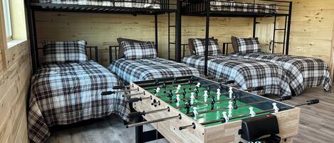 A room with bunk beds, a foosball table, and wooden flooring.