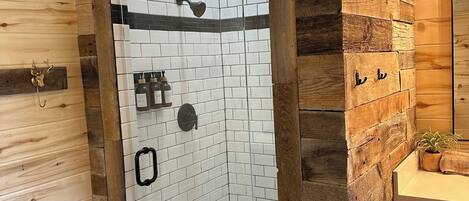 Ducha con puerta de vidrio, azulejos blancos y suelo con diseño de espiga.