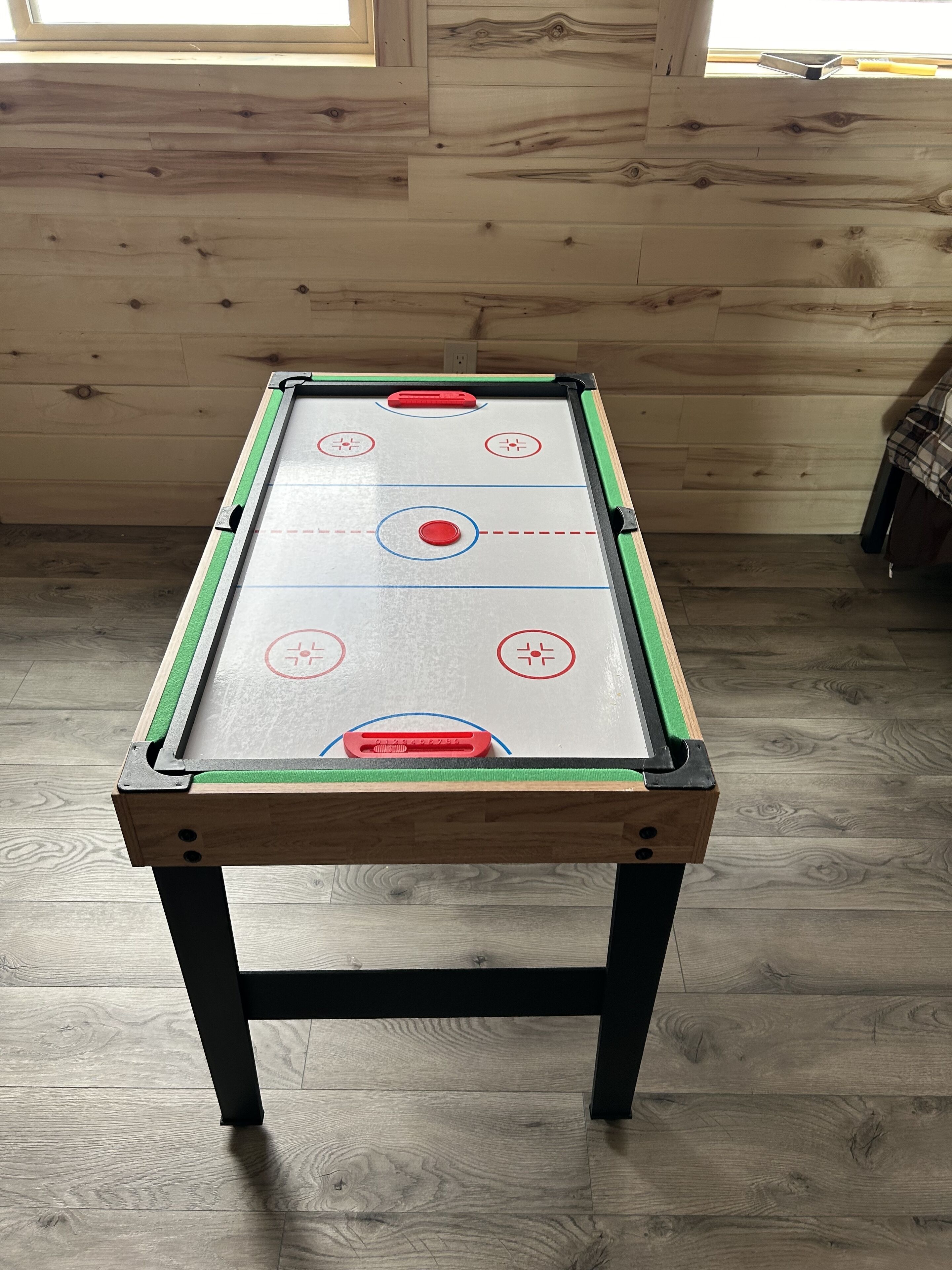 Una mesa de billar con estructura de madera, tapete verde y superficie blanca con marcas rojas y azules.