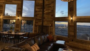 Ein Interieur einer Blockhütte mit Essbereich, einem Ledersofa und großen Fenstern mit Blick auf die Landschaft.