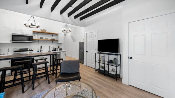 Uma cozinha moderna com uma ilha central, banquetas de bar, uma mesa de centro de vidro e uma TV sobre um suporte preto.