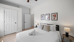 Quarto de hotel com uma cama grande, duas mesas de cabeceira com luminárias, uma porta e três quadros na parede.