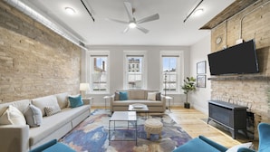 A modern living room with a brick wall, a sofa, a coffee table, and a fireplace. - Huge Retreat| Rooftop Deck| Stay At Findlay Market (Cincinnati)