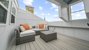 A rooftop deck with wicker furniture, a stone wall, and large windows offering a view of the sky. - Huge Retreat| Rooftop Deck| Stay At Findlay Market (Cincinnati)