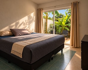 A bedroom with a large bed, a view of a garden through a sliding door, and a chair outside.