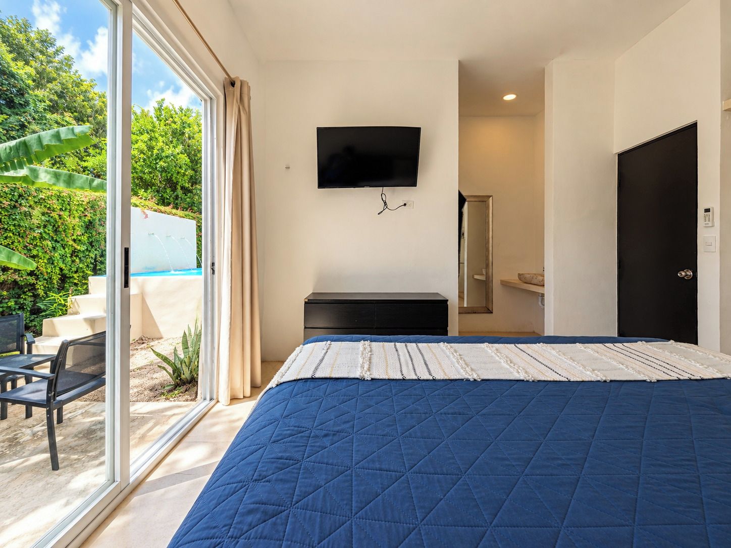 A bedroom with a large bed, a TV mounted on the wall, and a view of a swimming pool outside.
