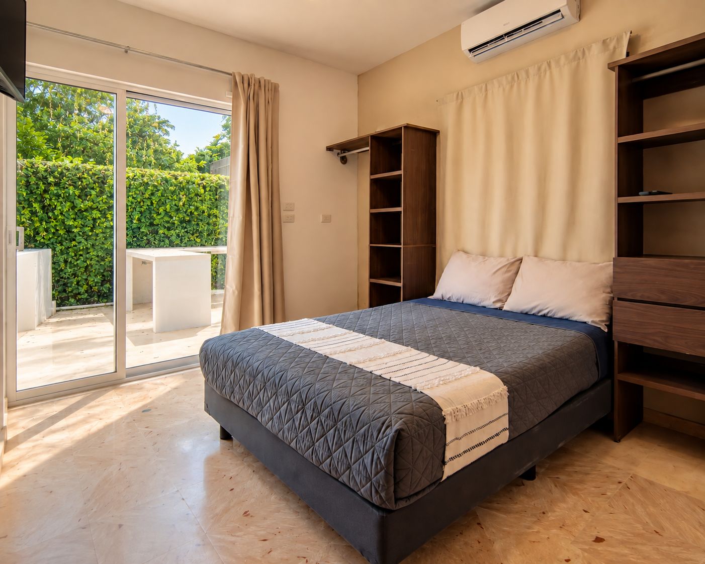 Een slaapkamer met een bed, een inbouwkast, een schuifpui naar een balkon en een airconditioningsysteem.