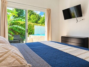 A bedroom with a bed, a TV, and a view of a pool and greenery.
